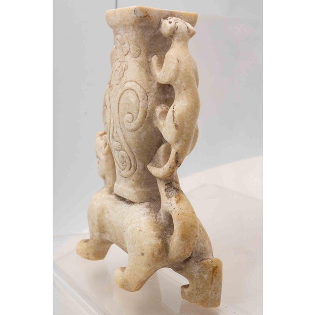 A striking vintage Chinese hand-carved stone vessel depicting a mythical beast supporting a decorative vase form. The...