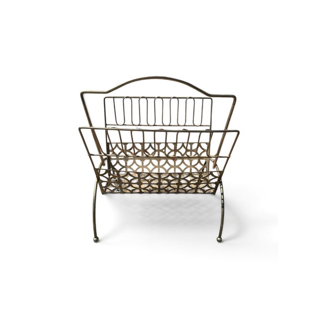 A handsome mid-century modern magazine rack in brass-toned metal, blending airy wireframe construction with a decorative...