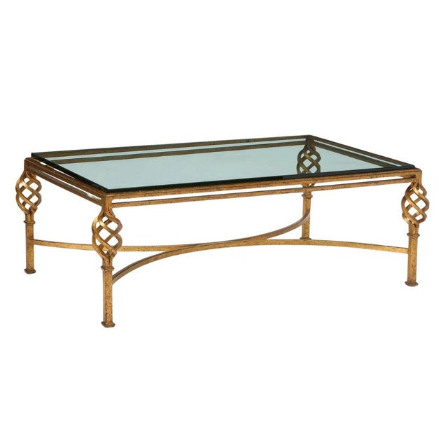 A Hollywood Regency style coffee table featuring an elegant gilt iron base and inset glass top. Each corner is adorned...