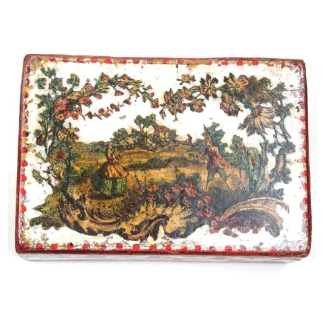 The papier mâché box depicting a landscape scene on a white ground with red trim on all sides. Made in the mid 18th century.