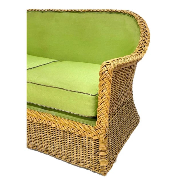 Vintage green upholstered wicker loveseat with two removable seat cushions with contrast brown/ white cording. Braided...