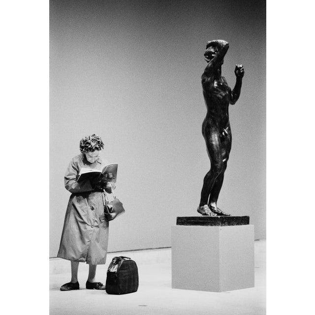 The Age Of Bronze A woman reads a catalog while standing next to the bronze cast 'The Age of Bronze' by Auguste Rodin at...