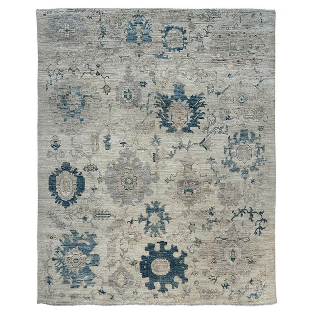 Oversized denim blue and deep teal flowers stand out against the ivory ground of this handmade Oushak wool rug. Pale gray...