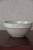 A traditional French ironstone bowl in a creamy off-white glaze, with a wide flat rim, slightly rounded body and footed...