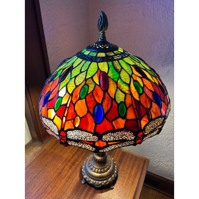 Beautiful Tiffany style leaded stained glass dragonfly table lamp. Rich shades of red, orange, and green with blue and...