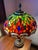 Beautiful Tiffany style leaded stained glass dragonfly table lamp. Rich shades of red, orange, and green with blue and...