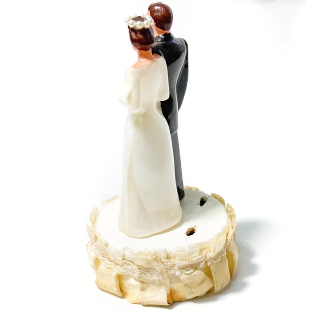 A beautiful vintage mid-century wedding cake topper featuring a classic bride and groom standing together on an ivory...