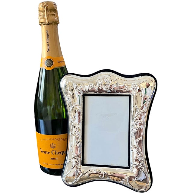 An elegant silverplated picture frame embellished with raised flowers, curling stems, and flowing foliage. Its gently...