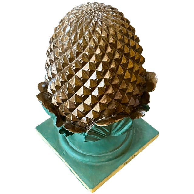 A striking architectural accent featuring a gold-toned pinecone form nestled within a collar of sculpted turquoise leaves....