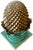 A striking architectural accent featuring a gold-toned pinecone form nestled within a collar of sculpted turquoise leaves....