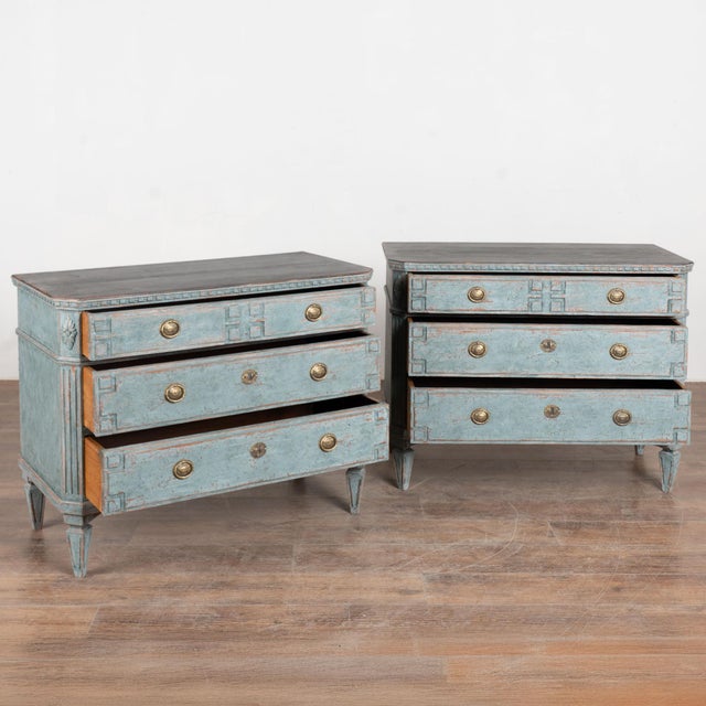 A pair of elegant Gustavian pine chests of three drawers painted in shades of blue and contrasting black top with simple...