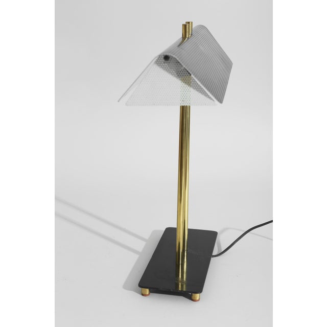 Linear desk lamp defined by a wide, angled shade with a ribbed surface, set on dual brass supports. The composition is...