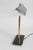 Linear desk lamp defined by a wide, angled shade with a ribbed surface, set on dual brass supports. The composition is...