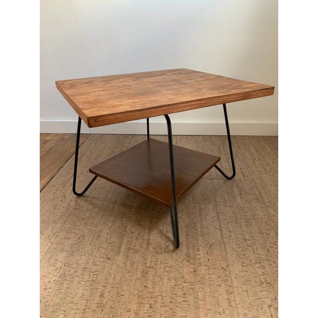 A vintage mid-century modern wood side table with two tiers and a swivel top. The table features hairpin style iron legs...