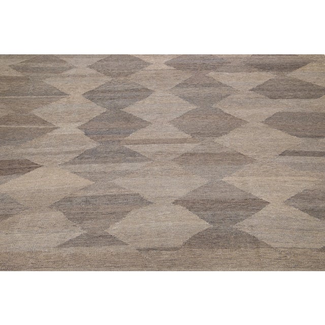 This wool flatweave Kilim rug is enhanced with a captivating brown color field and grey highlights throughout. Its...