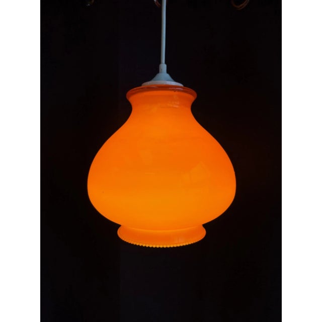 Elegant vintage pendant light in orange opaline, typical of 1970s design. Its curved shape and vibrant color add a pop of...