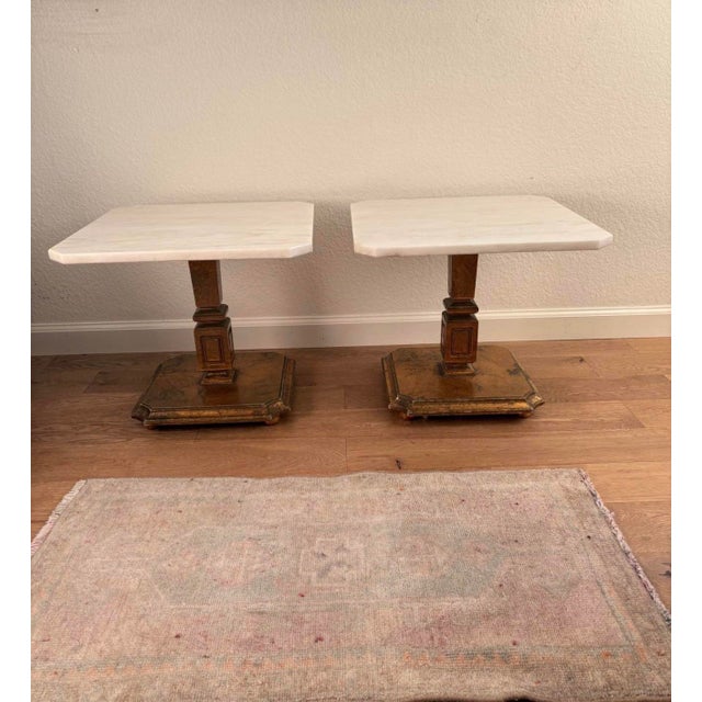 Elegant matching pair of vintage Hollywood Regency style pedestal tables featuring substantial white marble tops and...