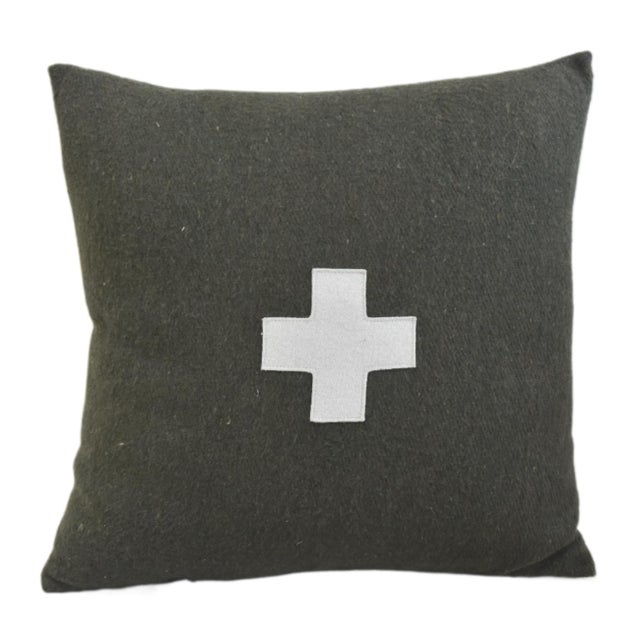 Custom-tailored pillow created from a dark green wool textile. Pillow has a cream-colored wool appliqué cross on the...