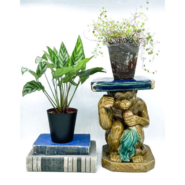 Vintage ceramic monkey plant stand featuring a seated monkey supporting a rectangular platform above its head. The monkey...