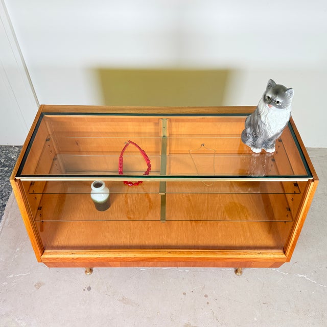 A charming cabinet that can serve as either a compact counter or a low display case. The unit stands on gold-colored legs...