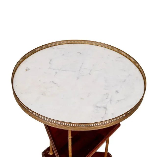 A vintage round marble top gueridon table with a brass rail, brass legs and mahogany shelves. At the heart of this...