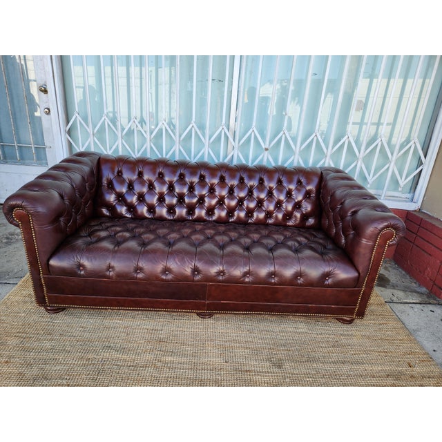 Classic Chesterfield sofa in dark brown leather. This piece has deep button tufting across the back, seat, and rolled...