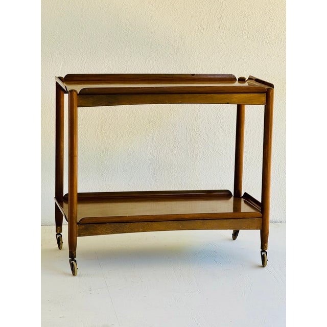 A two-tier folding trolley. The removable trays of bent walnut fit into a folding bases with brass hinges. Stamped “Made...