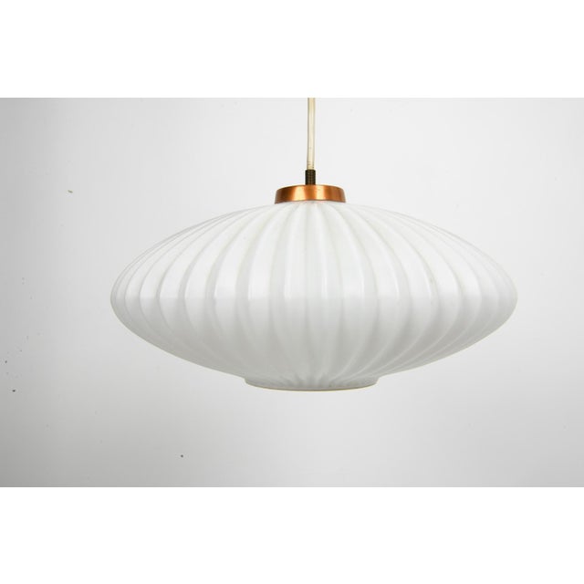 A sculptural vintage pendant attributed to Louis Kalff for Philips, combining a broad ribbed glass shade with a warm...