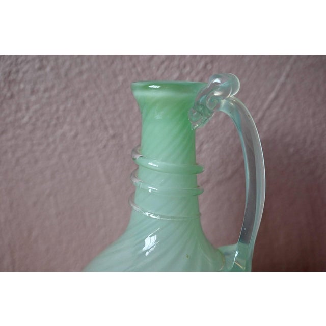 Soft and luminous, this antique hand-blown glass carafe captivates with its opaline seafoam green hue, a delicate, pearly...