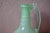 Soft and luminous, this antique hand-blown glass carafe captivates with its opaline seafoam green hue, a delicate, pearly...