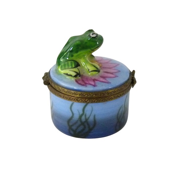 This tiny hand painted Limoges trinket box features a plump green frog perched atop a vibrant pink water lily floating in...