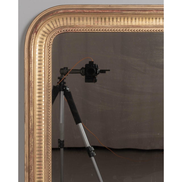 A 19th century French Louis Philippe style gilded mirror with curved top corners, incised ribbed decoration and inner bead...