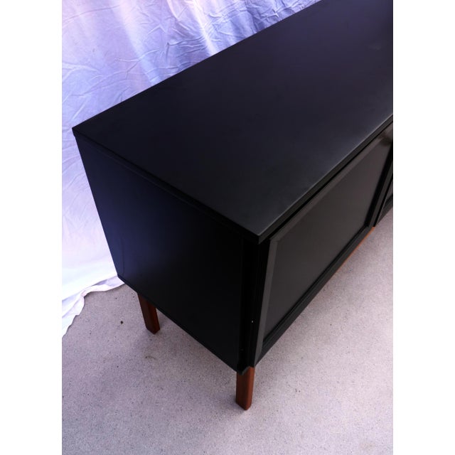 Large black sideboard with three doors, one of which opens to reveal three drawers. Solid teak legs. The two doors lock.