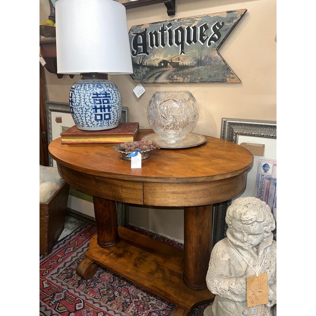 Antique early 1900s library table. Distinctive oval shape with double pedestal base, lower display shelf, and single...