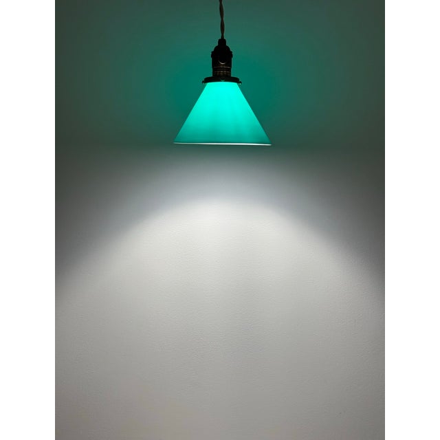 Vintage pendant light featuring a deep green translucent glass shade paired with a warm antiqued brass socket assembly....