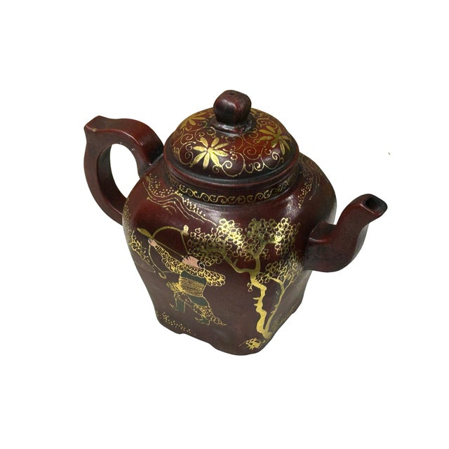 This is an Oriental reddish-brown clay teapot featuring rich, golden graphic detailing. The squat, somewhat angular body...