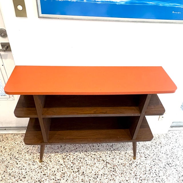 A vintage wood grain laminate display or storage shelf, with orange painted wood top and tapered spindle legs. Good...