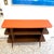 A vintage wood grain laminate display or storage shelf, with orange painted wood top and tapered spindle legs. Good...