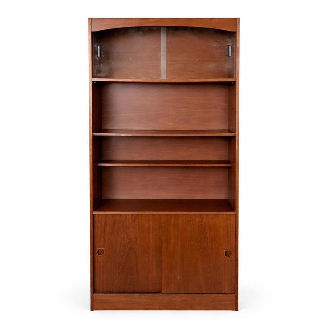 A classic mid-century Danish teak bookcase cabinet, combining elegant open shelving with practical concealed storage....