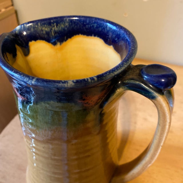 Stunning handmade pottery pitcher in blue, brown, dark brown, pink and a tan glaze. Thumb rest crafted on top of handle...
