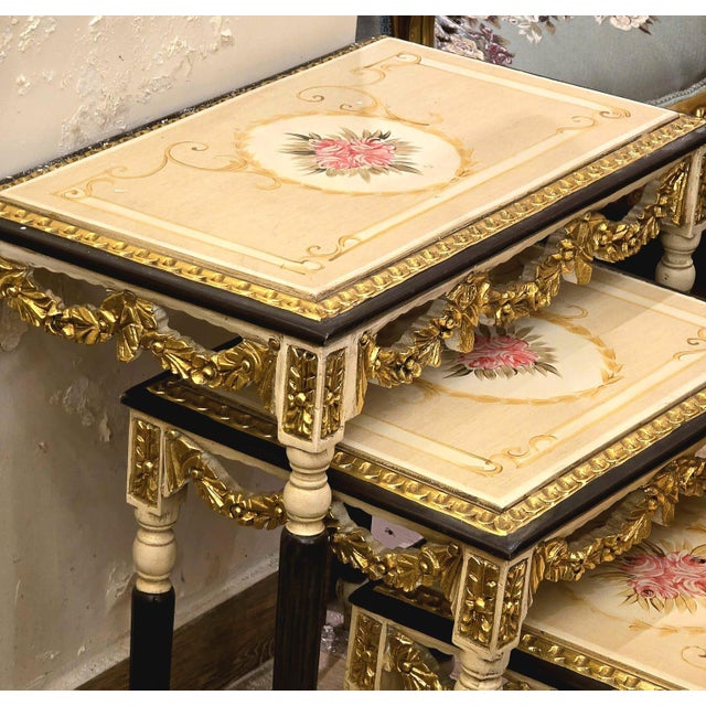 Elegant set of three French-style nesting tables featuring sophisticated black frames accented with luxurious gold leaf...
