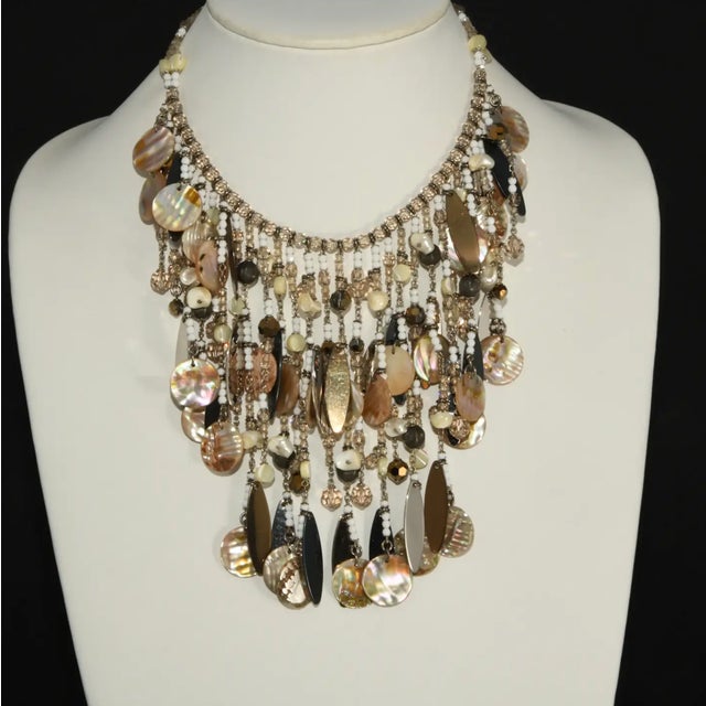 Waterfall bib necklace filled with dangles comprised of mother of pearl discs, small shells, Swarovski crystal beads, and...