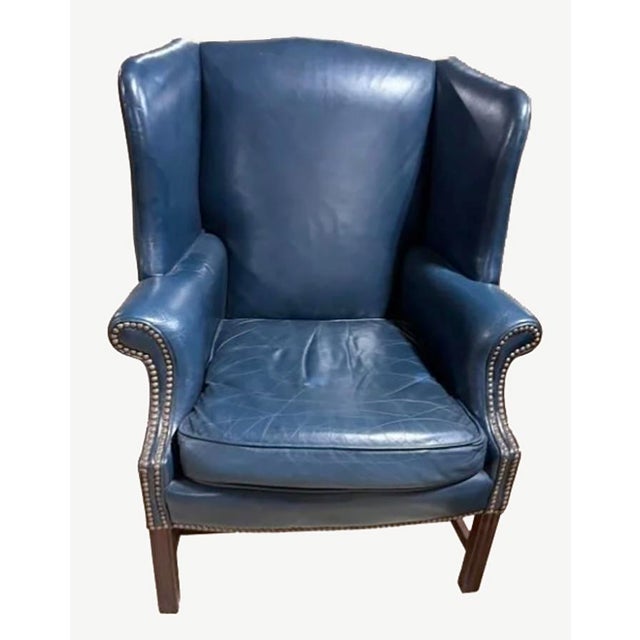 A handsome pair of traditional wingback chairs upholstered in rich navy blue leather, featuring classic rolled arms, brass...