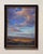 This pastel work captures a vast, open landscape under a dramatic sky filled with vibrant clouds that transition from warm...