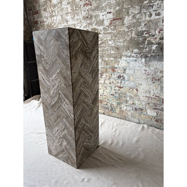 A striking rectangular pedestal clad in richly variegated gray stone arranged in a bold herringbone pattern. Layers of...