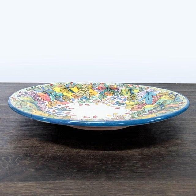 The plate features a hand-painted floral design with vibrant colors and a blue rim. Brand: Rampini Radda Ceramics....