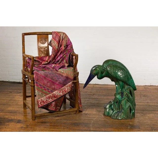 A vintage Chinese ceramic life size heron bird sculpture from the Mid-20th Century, with green glaze, blue accents and...
