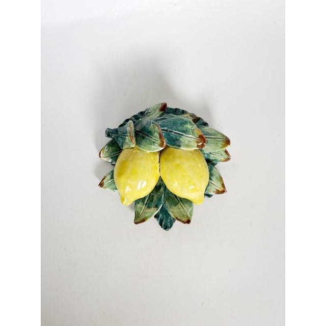 A charming decorative glazed ceramic sculpture featuring a pair of yellow lemons surrounded by abundant foliage in various...