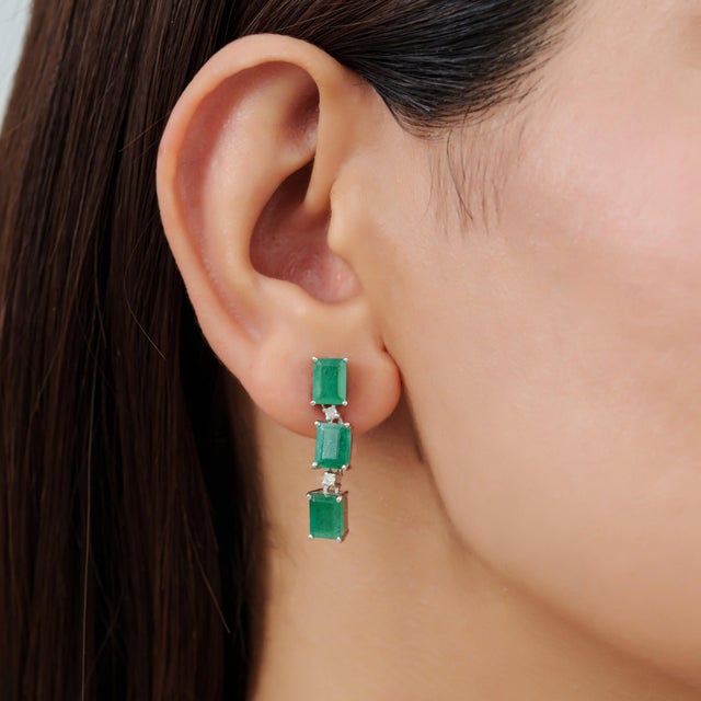 Elegant Art Deco-inspired dangle earrings featuring 6.32 carats of natural octagon-cut emeralds arranged in a refined...