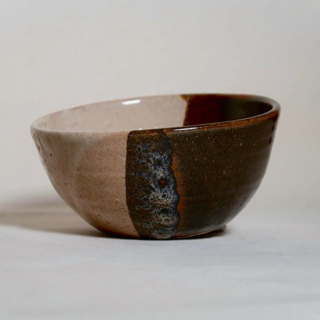 This hand-thrown studio pottery bowl features a classic, gently rounded form accented by a striking split-glaze...